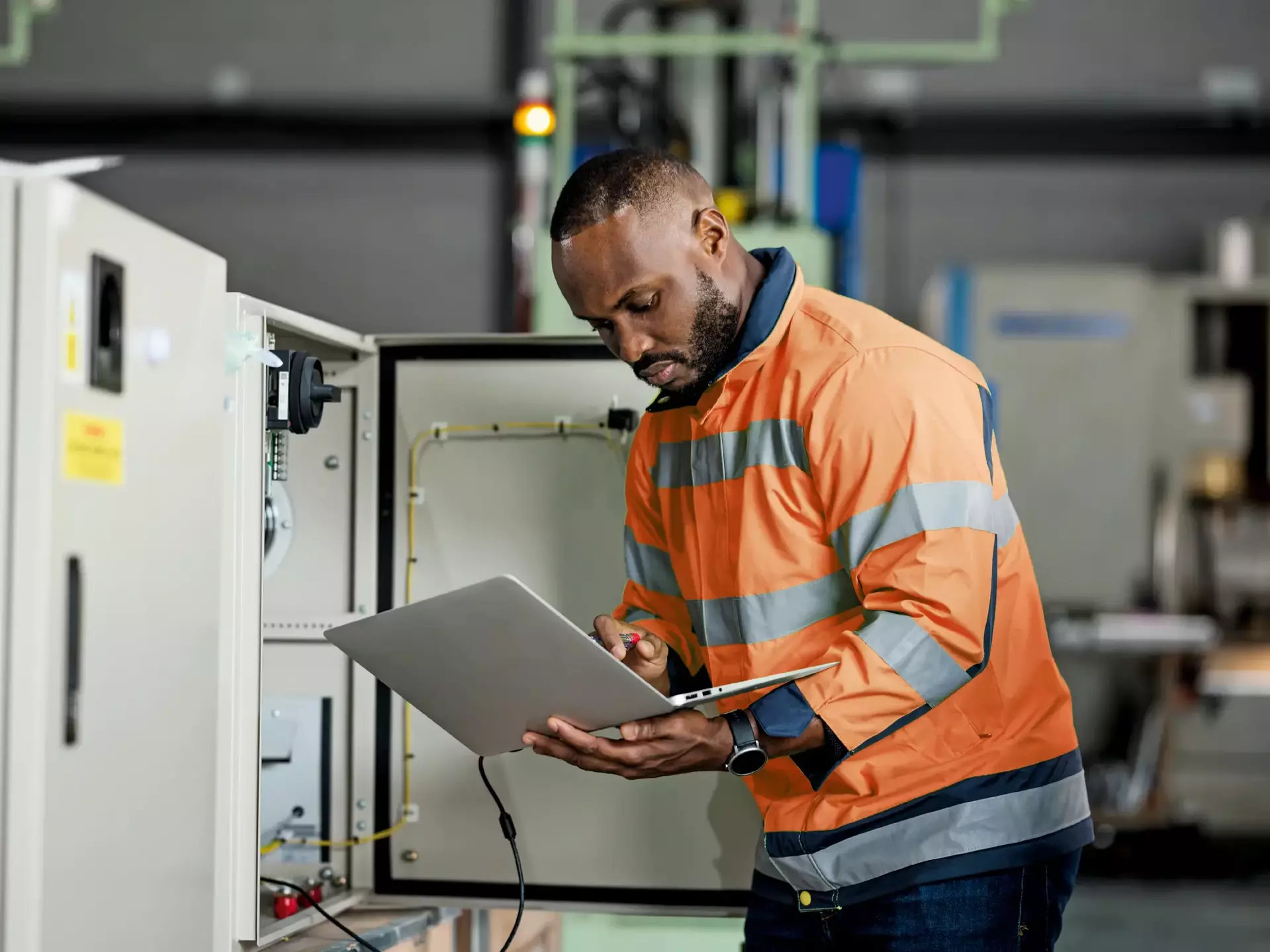African electrician engineer is examining and testing complex equipment by a laptop in a circuit cabinet of the solar cell power storage African electrician engineer is examining and testing complex equipment by a laptop in a circuit cabinet of the solar cell power storage