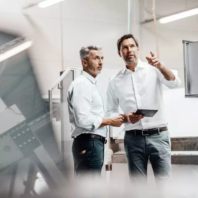 Male engineer with digital tablet pointing while discussing with colleague in manufacturing industry