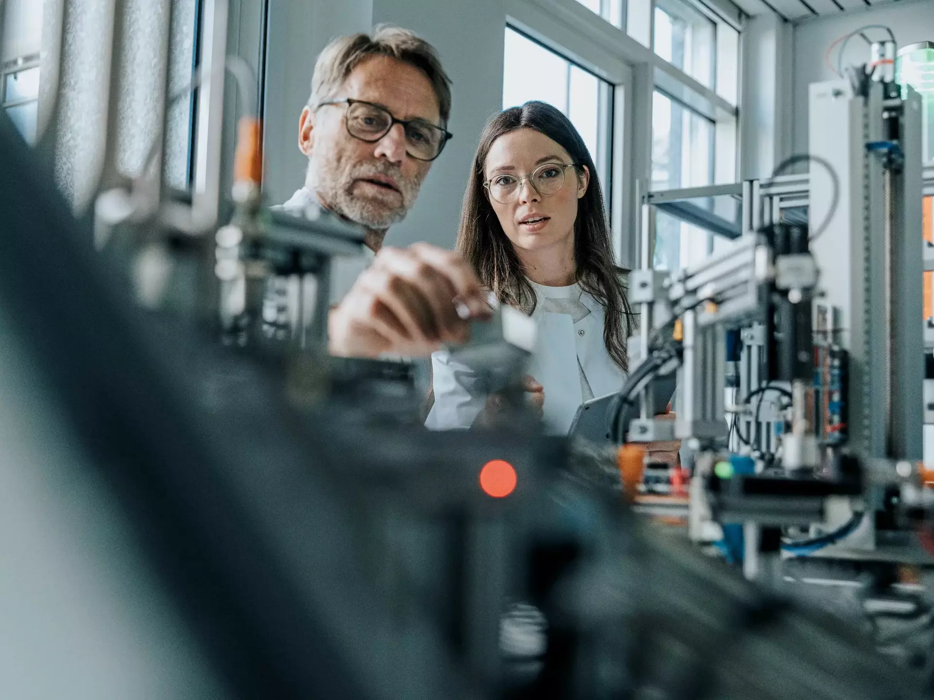 Männlicher Wissenschaftler mit junger Frau, die Maschinen im Labor untersucht