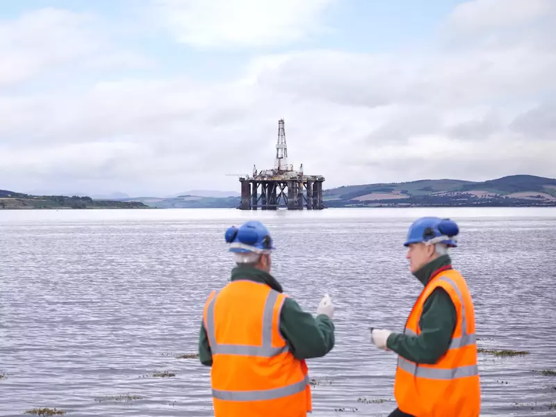 Two male oil worker on shore with oil rig in background Two male oil worker on shore with oil rig in background